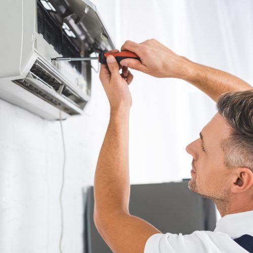 handsome adult man repairing air conditioner with screwdriver